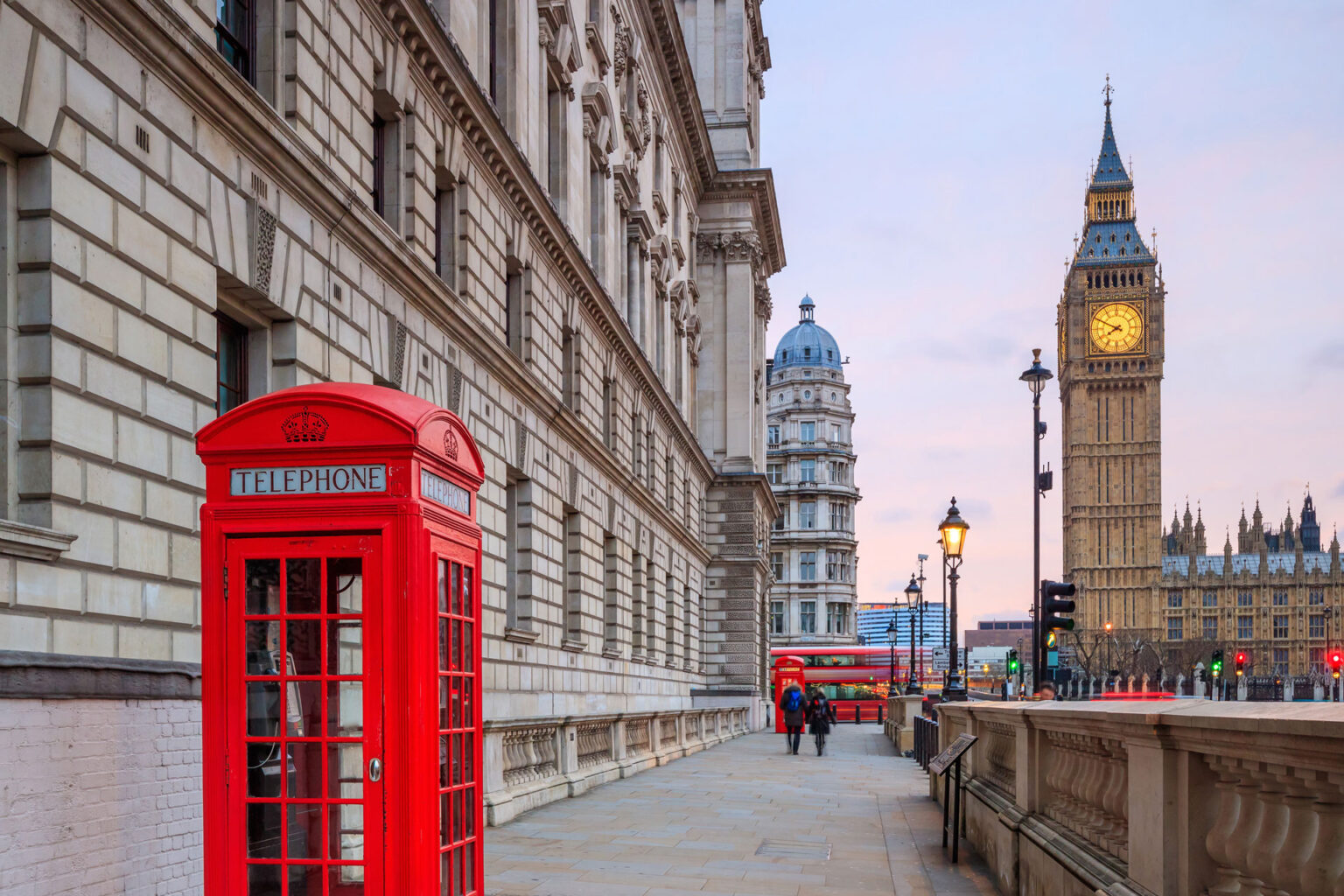 A red telephone booth on the side of a street.